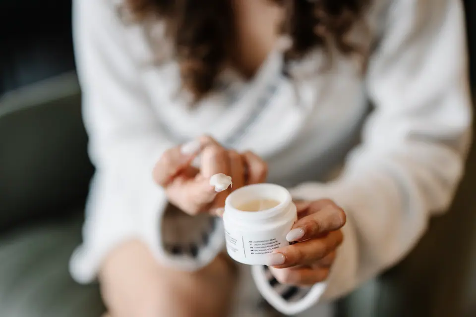Persona con un sweater abrigado aplicándose crema de un frasco en las manos