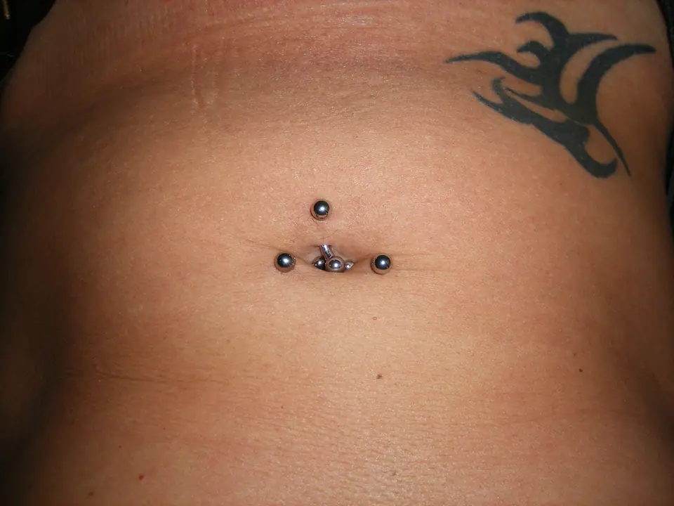 Piercing de ombligo con barra curva, cicatriz de tatuaje cerca