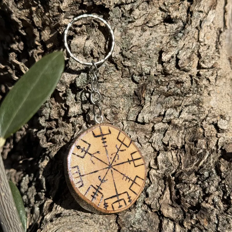 Llavero de madera de olivo tallado con el símbolo vegvísir, colgado de la corteza de un árbol